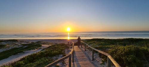 a person walking down a boardwalk to the beach at sunset at Casa Pescador Beach House in Struisbaai