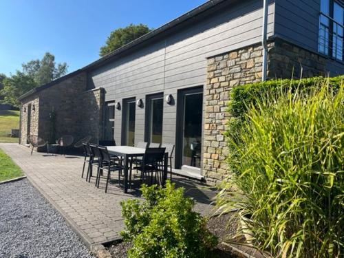 a patio with a table and chairs next to a building at Les midis au vert - Les Loges - 11 personnes in Stavelot