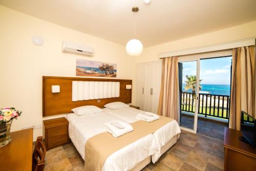 1 Schlafzimmer mit einem Bett und einem Balkon mit Meerblick in der Unterkunft Kefalos Beach Tourist Village in Paphos City
