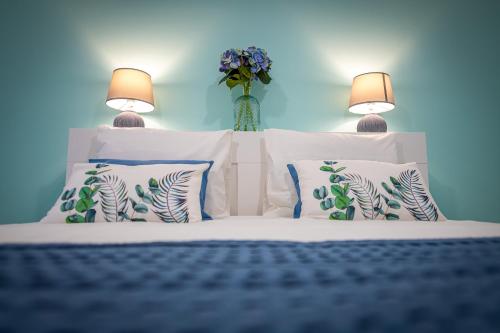 1 cama con almohadas blancas y un jarrón con flores en Dimore Italiane - Boutique Apartments en Corralejo