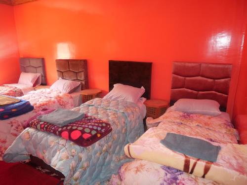 a room with three beds and an orange wall at Maison D'hôtes Chez Bassou Agoudal in Agoudal