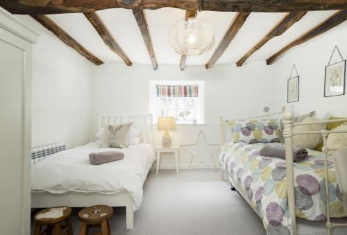a white bedroom with two beds and a chandelier at Corner Cottage in Adlestrop