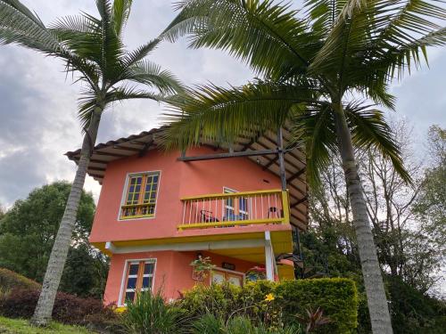 a pink house with a balcony and two palm trees at Cabañas y Flores in Jericó