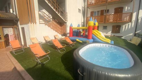 un patio trasero con piscina con sillas y parque infantil en Hotel Olisamir, en Cavedago