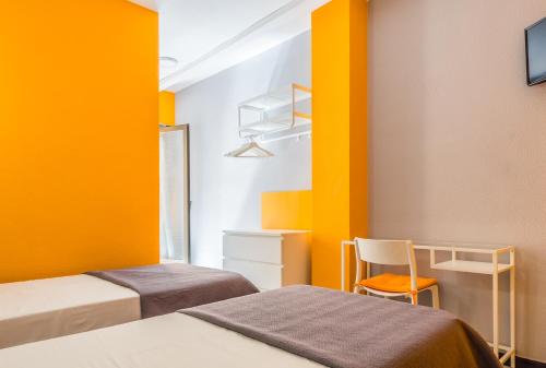 two beds in a room with yellow walls and a chair at Hostal Tropical in Almuñécar