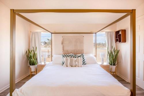 a large white bed in a bedroom with windows at Hemingway House - Hot Tub Under The Desert Stars in Yucca Valley