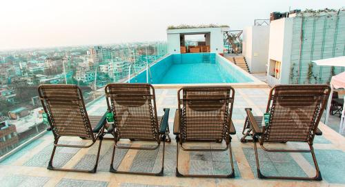 3 Stühle auf einem Gebäude mit Pool in der Unterkunft Royal Raj Hotel in Rajshahi