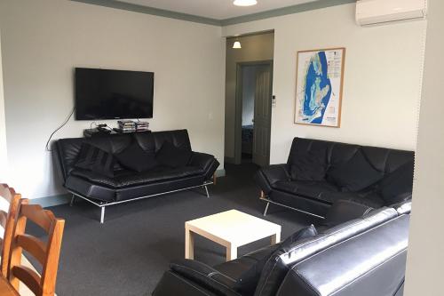a living room with black leather couches and a flat screen tv at By The Bay in Queenscliff