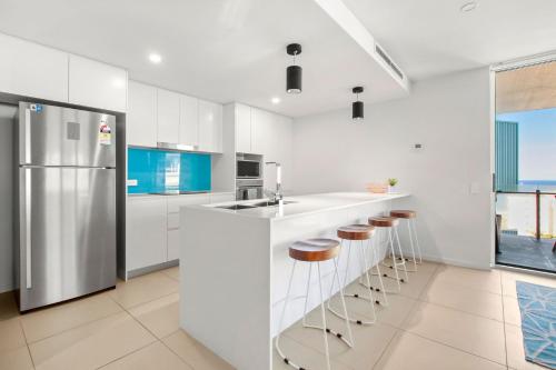 a kitchen with white cabinets and a refrigerator and stools at Aquaview Unit 304 Kings Beach in Caloundra