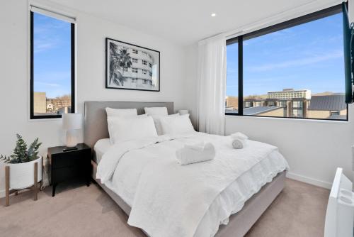 a white bedroom with a large bed and large windows at Top Floor Luxury City Central w Sunny Balcony in Christchurch