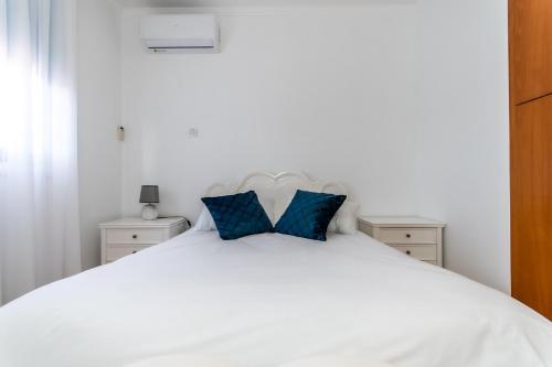 a white bed with two blue pillows on it at Reel Paradise Villa, Cyprus in Larnaka