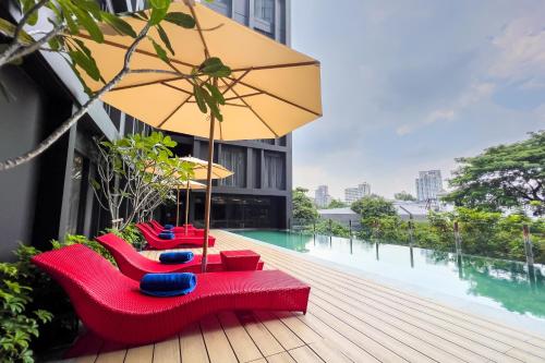 a deck with red chairs and an umbrella and a pool at Oakwood Studios Sukhumvit Bangkok in Bangkok