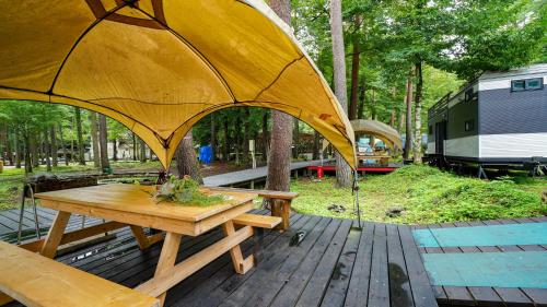 a wooden picnic table with a large yellow umbrella at 森と湖の楽園ＷorkshopＣampＲesort in Fujikawaguchiko