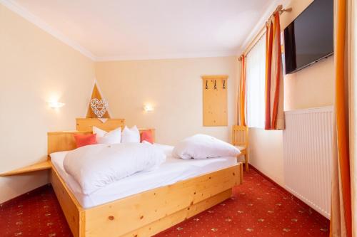 a bedroom with a bed with white sheets and a television at Alpenpension Elferblick in Neustift im Stubaital