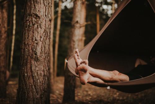 a person laying in a hammock in a forest at Jurty z widokiem, prywatna balia- DZIKOLAS GLAMPING in Krasnobród