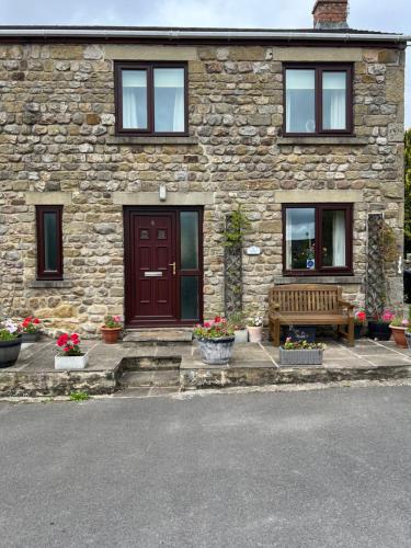 a stone house with a wooden door and a bench at Woodside Cottage in Ripon
