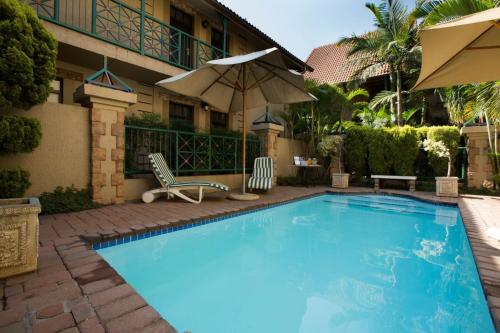 een zwembad met 2 stoelen en een parasol bij Court Classique Suite Hotel in Pretoria