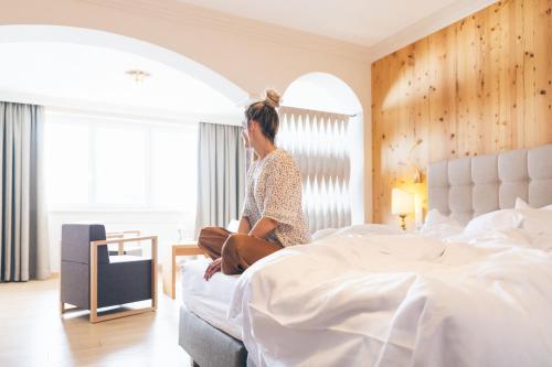 a woman sitting on a bed in a bedroom at Hotel Steiner Superior in Obertauern