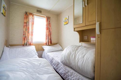a small room with two beds and a window at 6 Berth Caravan For Hire At Martello Beach Holiday Park In Essex Ref 29017y in Clacton-on-Sea