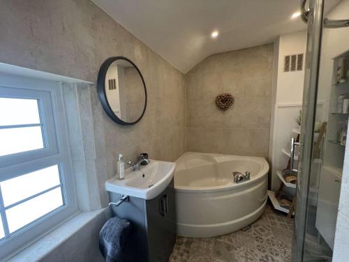 uma casa de banho com uma banheira, um lavatório e um espelho. em Old Smithy Cottage em Great Singleton