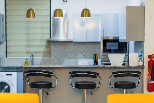 a kitchen with a counter with four orange bar stools at Cozy Apartments at East Airport in Burma Camp