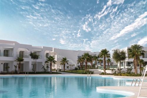 a large swimming pool in front of a building with palm trees at Meraki Resort Sharm El Sheikh Adults only in Sharm El Sheikh