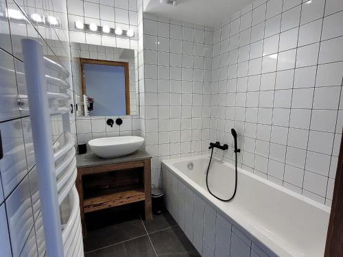La salle de bains est pourvue de carrelage blanc, d'un lavabo et d'une baignoire. dans l'établissement Appart charmant avec Jacuzzi, Terrasse, Parking & WiFi - FR-1-598-92, aux Gets