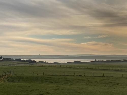 a field with a fence and a body of water at Loanside Lodge, Self-Catering, Holm, Orkney. in Saint Marys