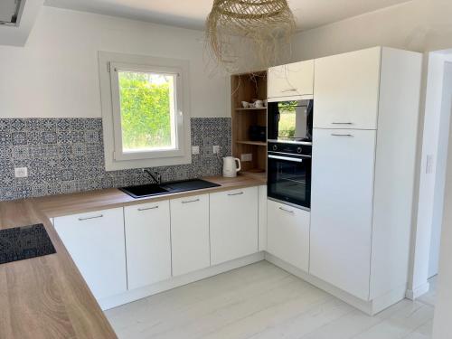 une cuisine blanche avec des armoires blanches et une fenêtre dans l'établissement Maison chaleureuse avec Jacuzzi, à Plouézec