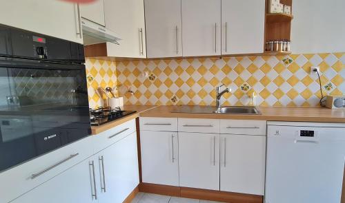 une cuisine avec des armoires blanches et des appareils noirs dans l'établissement Grande Maison dans le Bourg de Nevez + jardin, à Névez