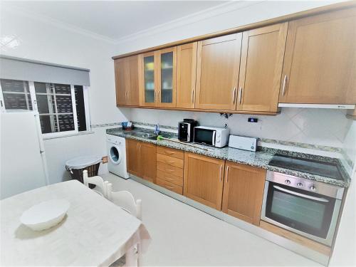 a kitchen with wooden cabinets and a white table and a table and a tablektop at Vivenda para férias (Algarve) in Manta Rota