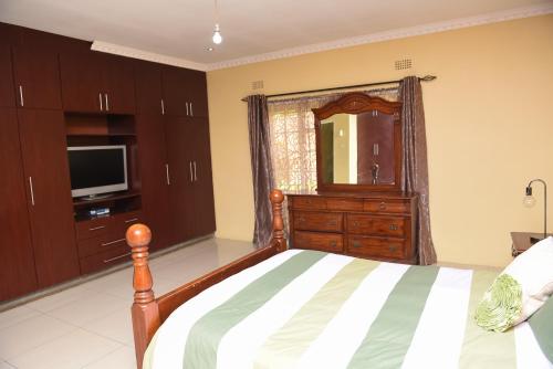 ein Schlafzimmer mit einem Bett, einem Spiegel und einem TV in der Unterkunft AZB Cozy Homes. Elegant 4 bedroom home in Area 49, Lilongwe in Lilongwe