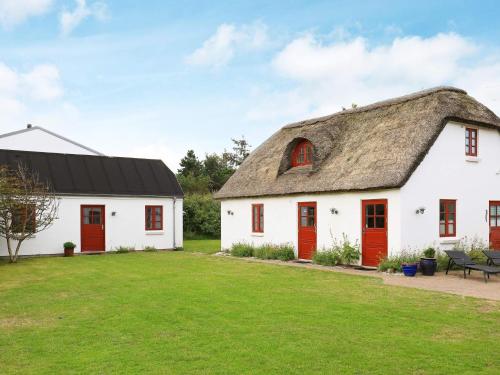 Cabaña con techo de paja, puertas rojas y patio de césped. en 8 person holiday home in Blokhus, en Blokhus