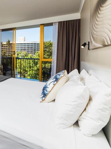 a bedroom with a bed with white pillows and a window at Pacific Hotel Cairns in Cairns