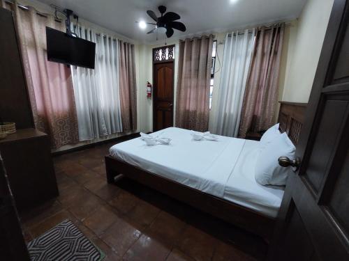 a bedroom with a white bed and a television at Makabata Guesthouse & Cafe in Manila
