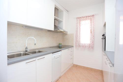 a kitchen with white cabinets and a sink and a window at Seaside family friendly house with a swimming pool Slatine, Ciovo - 17231 in Slatine