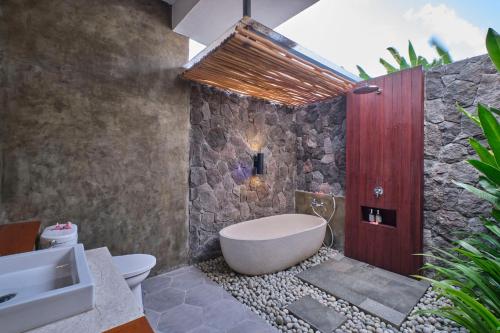 a bathroom with a white tub and a stone wall at Villa Casa Natura 15 - 2 BRV with private pool 15 mins to Ubud in Ubud