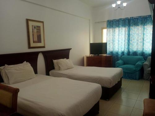 a hotel room with two beds and a chair at Oasis Hotel Apartment in Ras al Khaimah