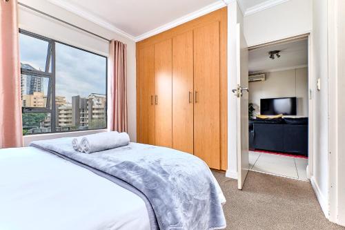um quarto com uma cama e uma grande janela em Westpoint Glammys Suites em Joanesburgo