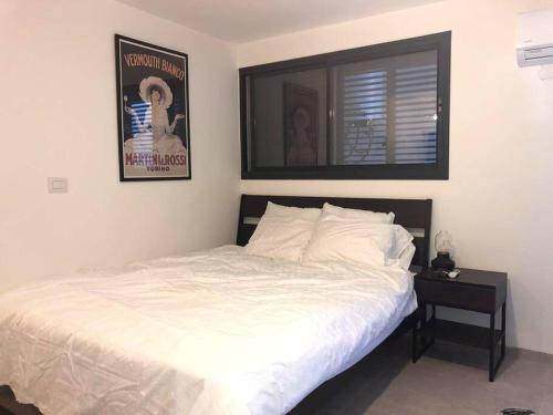 a bedroom with a white bed and a night stand at יחידה מושלמת ברמת ישי לזוג או יחיד in Ramat Yishay