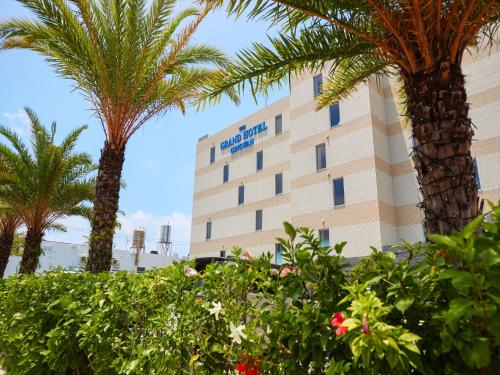 a hotel with palm trees in front of a building at THE GRAND HOTEL GINOWAN in Ginowan