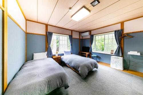 Guesthouse leaf في هوكوتو: سريرين في غرفة مع جدران ونوافذ زرقاء