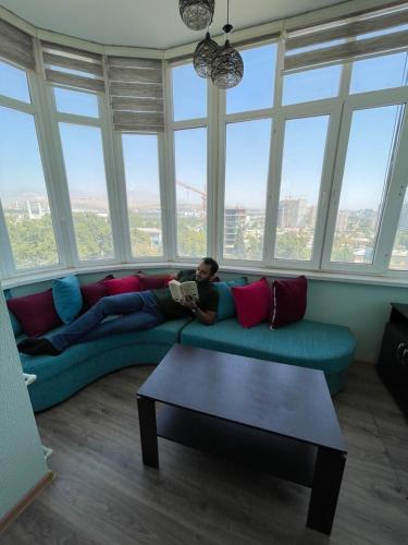 a man laying on a couch in a room with windows at Flamingo in Dushanbe