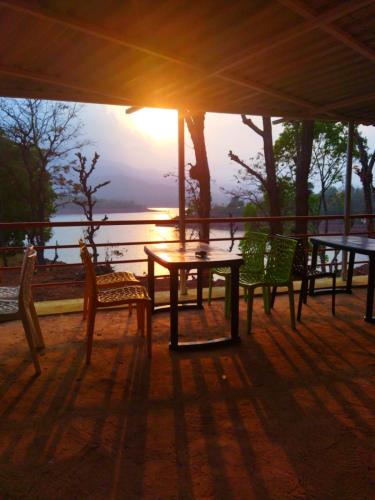 una mesa y sillas con la puesta de sol en el fondo en Omkar Agro Tourism & Resort, en Mahabaleshwar