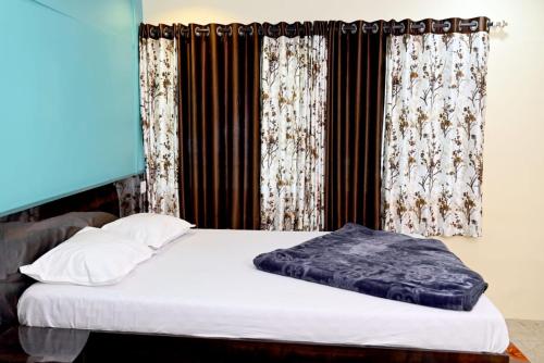 a bed with white sheets and a window with curtains at Omkar Agro Tourism & Resort in Mahabaleshwar