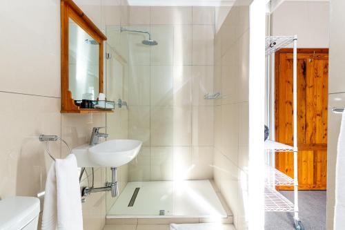 ein weißes Bad mit einem Waschbecken und einer Dusche in der Unterkunft Adventure Pad's by The Farmhouse Hotel in Langebaan