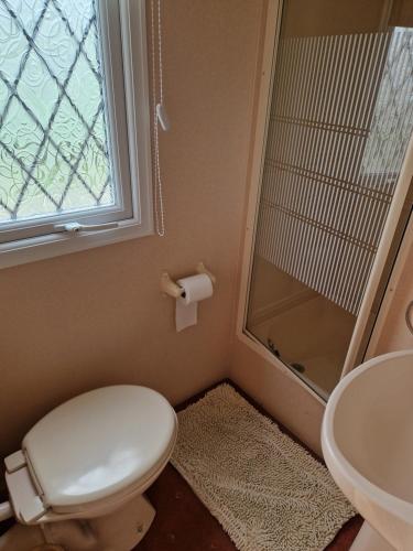 a bathroom with a toilet and a sink and a window at Corner pitch 4 berth caravan in Ingoldmells