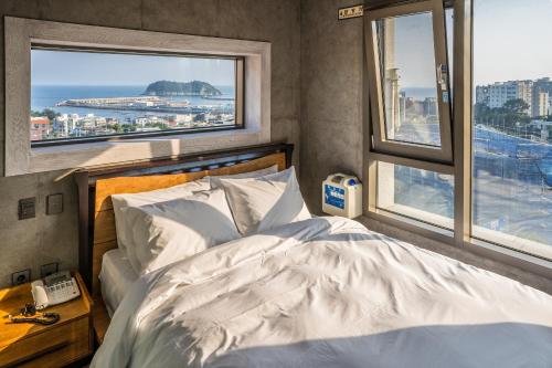 a bedroom with a white bed and two windows at Cornerstone Hotel in Seogwipo