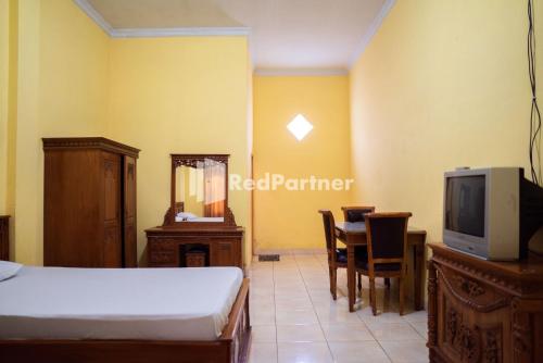 een slaapkamer met een bed en een televisie en een tafel bij Wisma Citra Metro Mitra RedDoorz in Banjarjo
