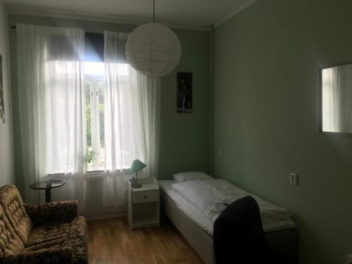 a bedroom with a bed and a chair and a window at Hunnebergs Gård Hostel & Camping in Vargön